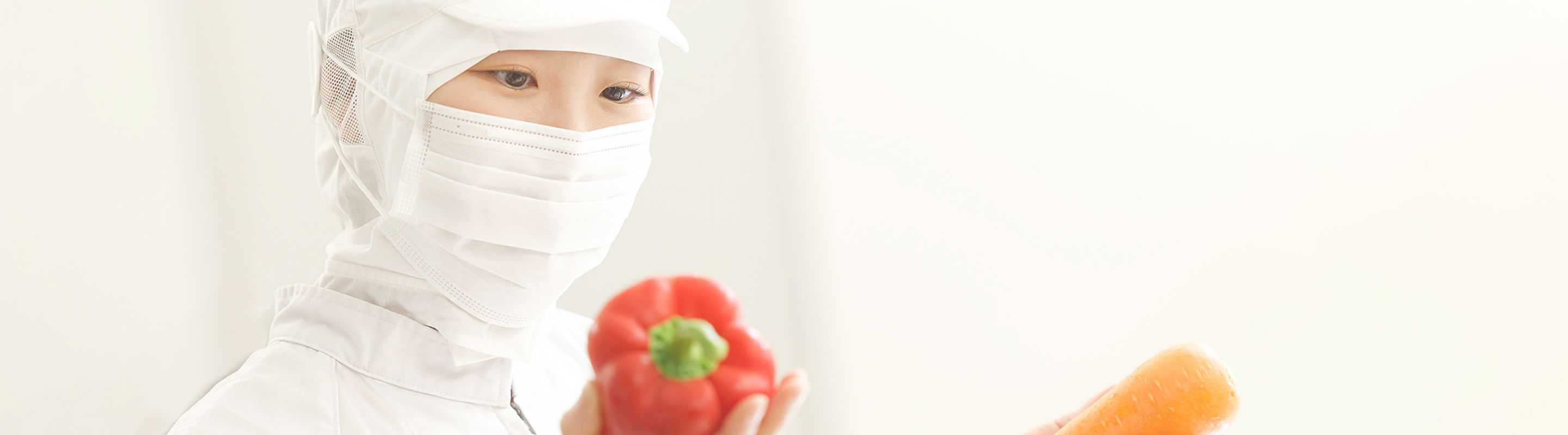 パプリカと人参を持ち真剣な顔で仕事をしている栄養士