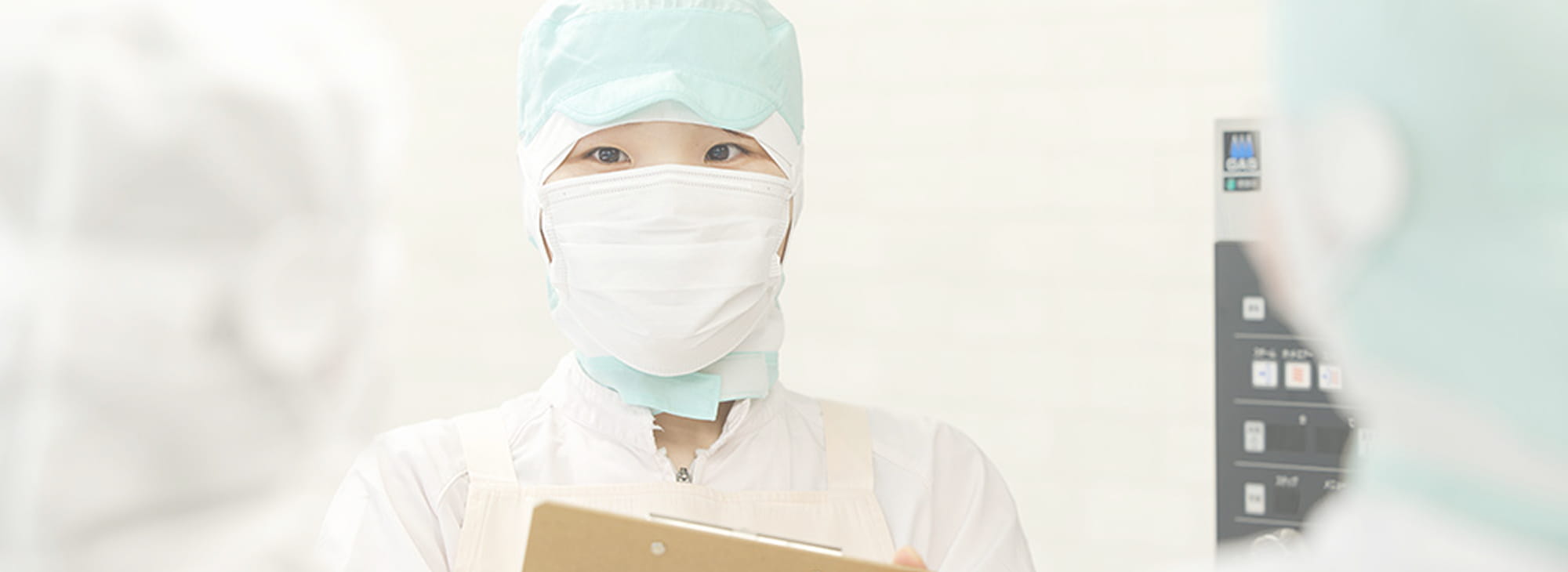 食品工場で記録作業を行う白衣とマスク姿の作業員