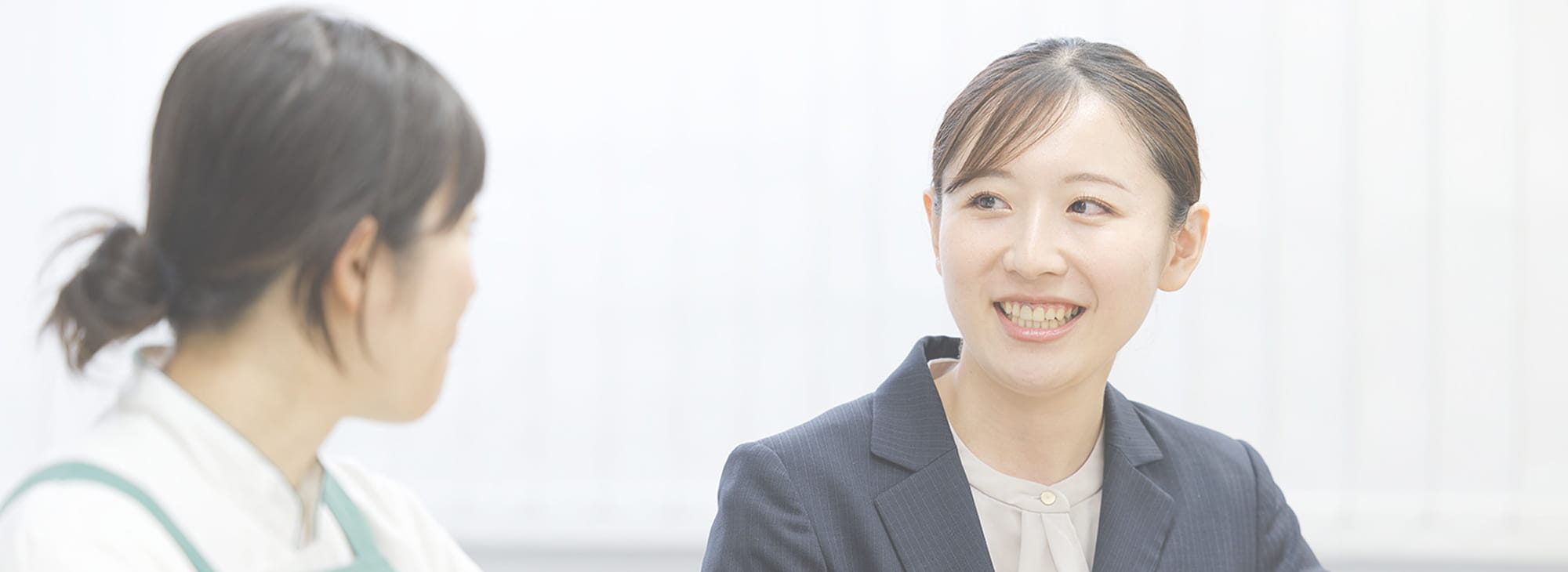 スーツ姿の女性がエプロン姿の女性と会話している様子