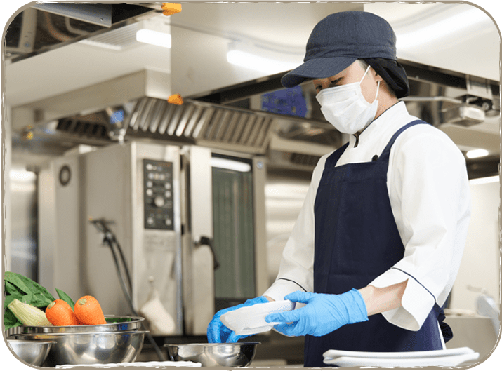 マスクと手袋を着用した女性がキッチンで料理をしている様子。