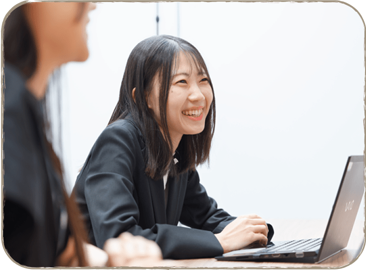 デスクに座り、ラップトップを使いながら微笑む女性の画像です。