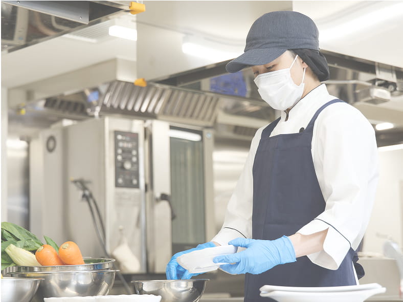 マスクと手袋を着用した女性がキッチンで料理をしている様子。