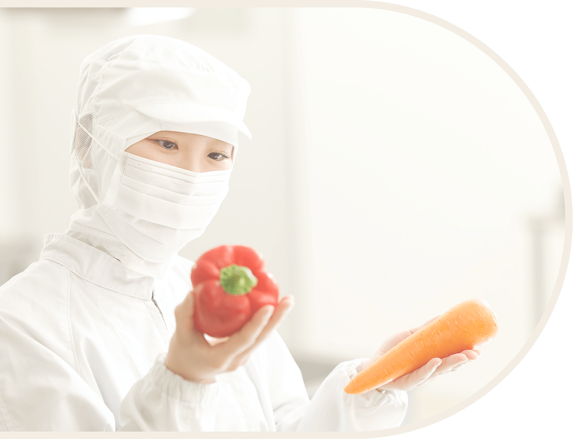 白い給仕服の女性が手にニンジンとパプリカを持っている様子です。